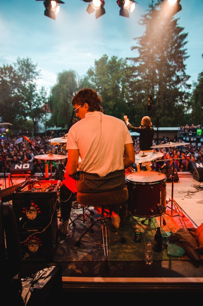 man wearing white top sitting in front of drum kit on concert